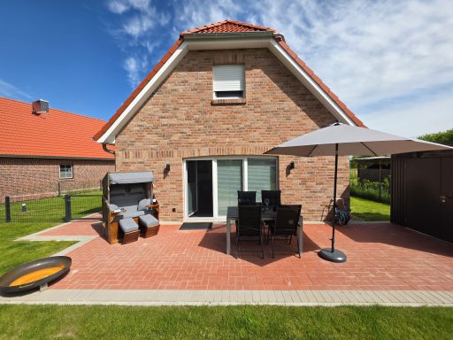 Moderne Terrasse mit Möbeln, Sonnenschirm und einem Gartenblick hinter einem Backsteinhaus.