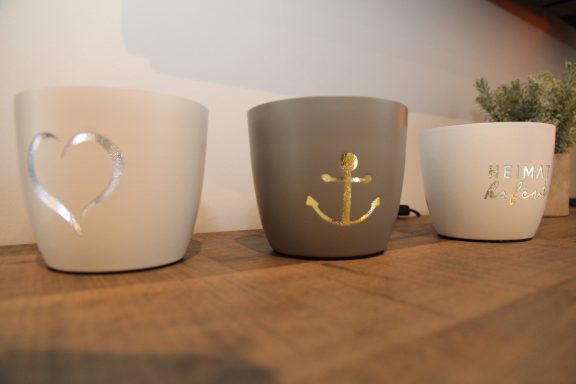 Drei Töpfe in verschiedenen Farben mit Motiven: Herz, Anker und ein weiteres Symbol.