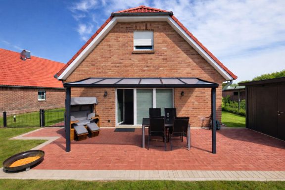 Gemütlicher Außenbereich mit Terasse und Gartenmöbeln hinter einem roten Backhaus.