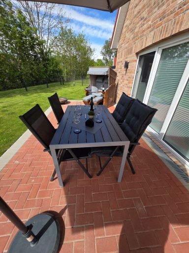Ein gedeckter Tisch mit Stühlen auf einer Terrasse, umgeben von Grün.