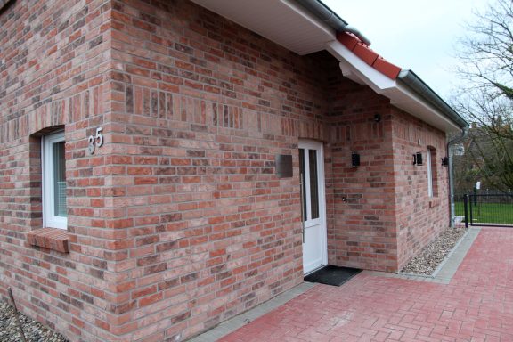 Ziegelsteinbau mit weißer Tür und gepflastertem Vorbereich.